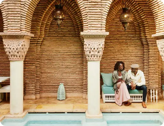 A couple sitting on a bench under sculptured arches of a building
